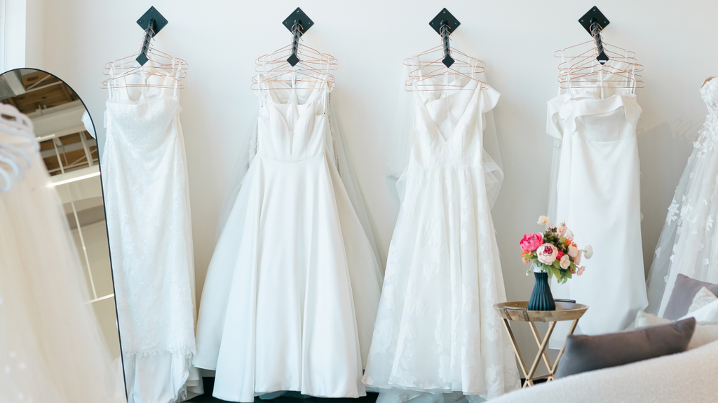Wedding dresses hanging in boutique with floral bouquet.