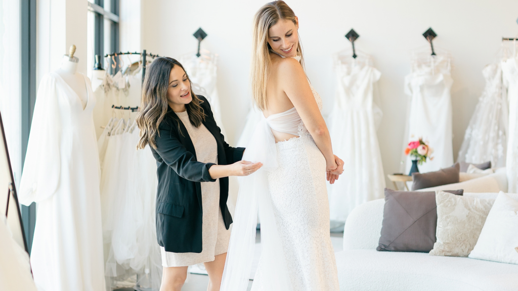 Owner, Irene, helping bride adjust bow on wedding dress.