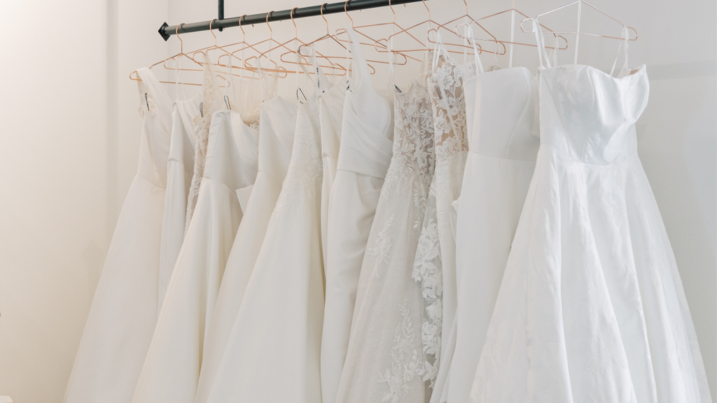 Justin Alexander wedding gowns hanging on a rack in boutique.